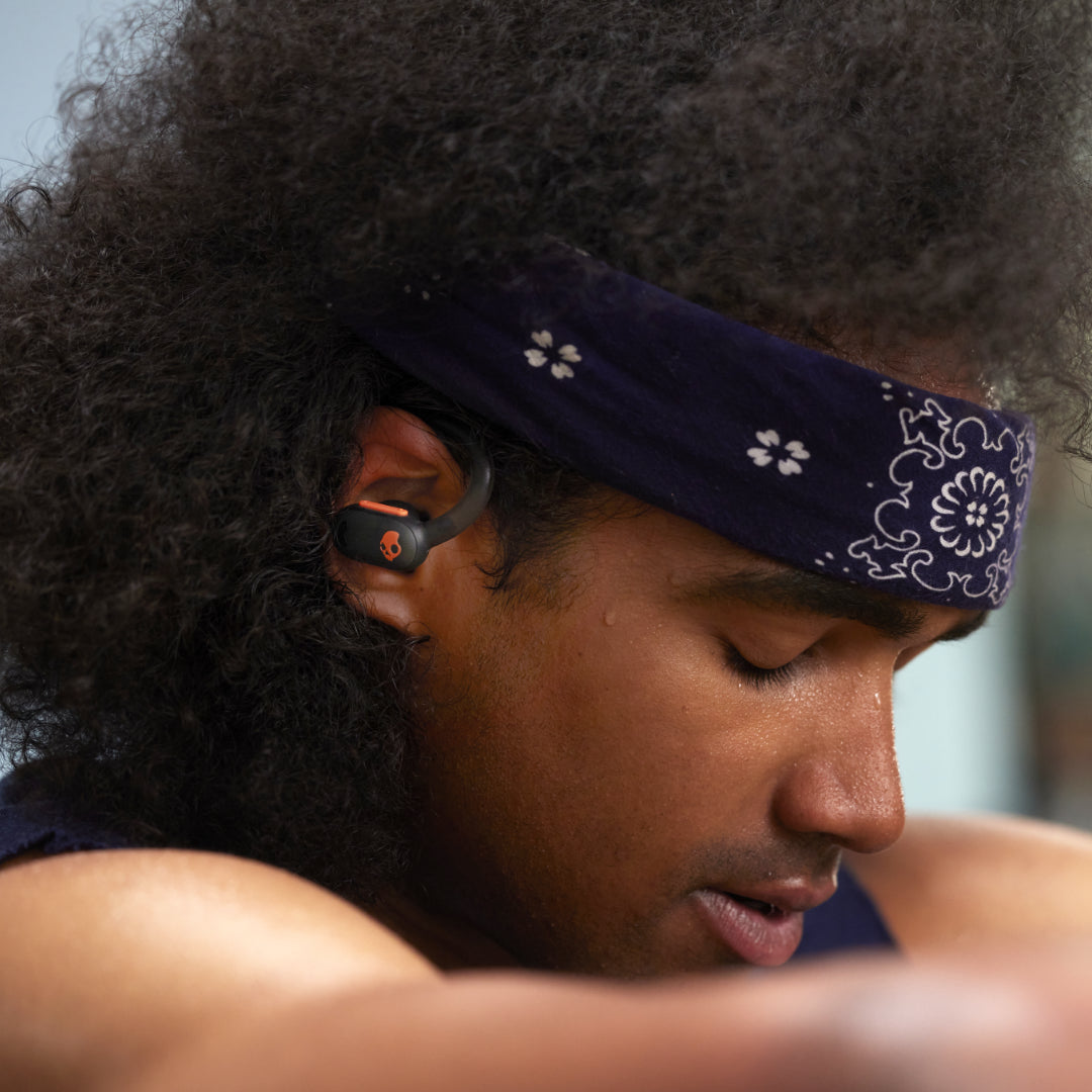 Young man in a tank-top and bandana listening to music with  Skullcandy wireless sport earbuds with flexible ear hooks